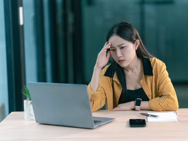 Asian call center woman is stressed from working with headphones, sitting and checking computer screen in the office.图片下载