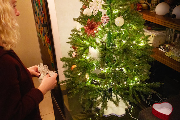 一个金发女子穿着红色毛衣，在室内装饰一棵绿色的仿真圣诞树。图片下载