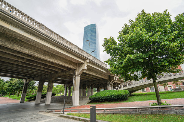 西班牙毕尔巴鄂市一座桥下的视角。背景中可见一座高耸的蓝色摩天大楼。照片拍摄于阴天，天空布满云层。图片下载