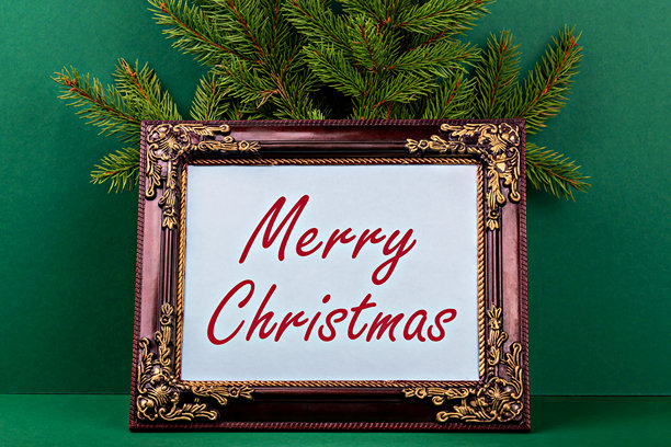 节日装饰画框，带有“圣诞快乐”的祝福语，背景为绿色，装饰有常青树枝图片下载