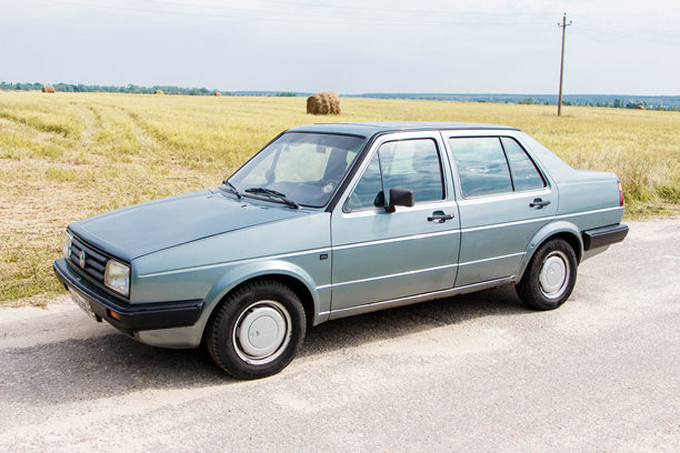 大众捷达二代停在乡村道路上，周围是金色的田野和蓝天，展现出经典的汽车设计和复古魅力图片下载
