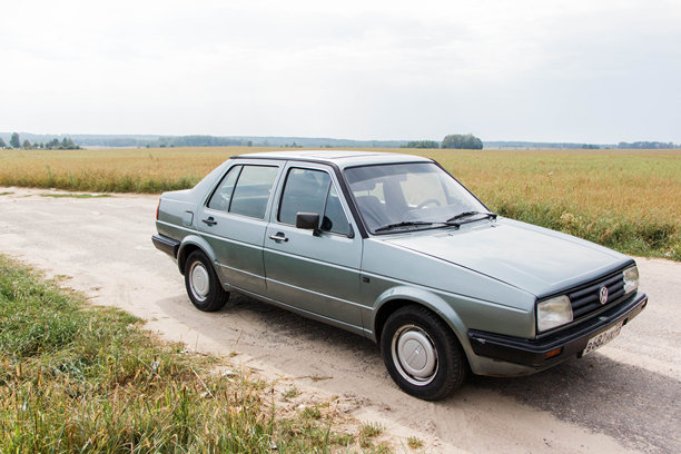 大众捷达二代停在乡村公路旁，周围环绕着郁郁葱葱的绿色田野，展现了经典的汽车设计和复古魅力图片下载