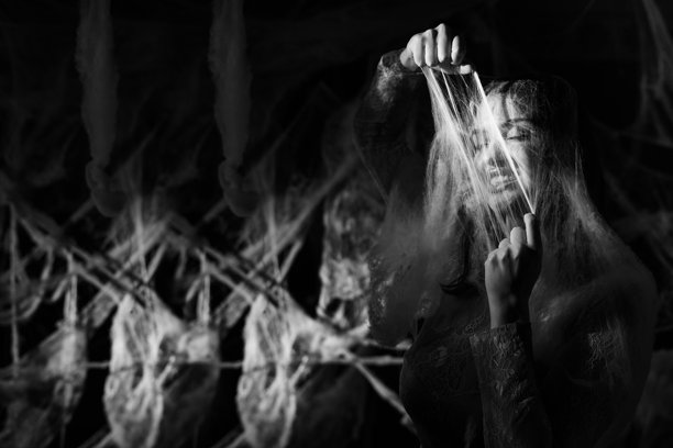 万圣节背景下，一个害怕的神秘女子被蛛网和蜘蛛网困住。黑白照片。图片下载