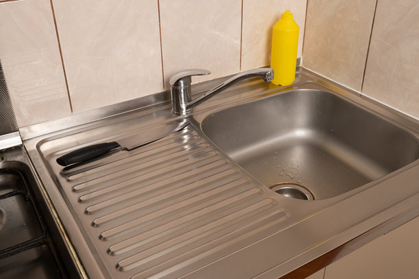 带瓷砖墙壁的厨房水槽，配有金属水龙头、刀具和黄色洗涤剂瓶。图片下载