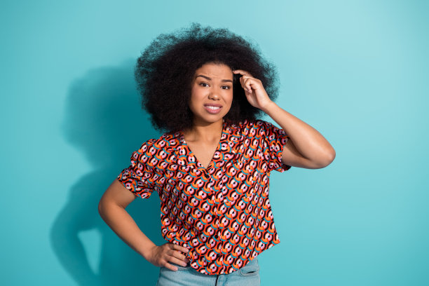 一位拥有蓬松发型的年轻女子，身穿大胆图案的衬衫，站在蓝色背景前，这是一张生活方式时尚图片图片下载