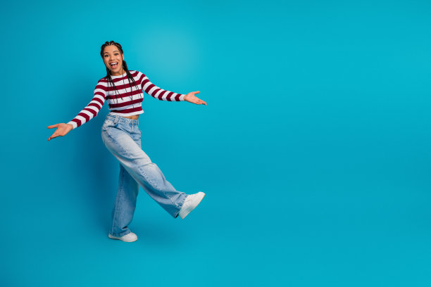 身穿条纹上衣和牛仔裤的年轻女模特在蓝色背景前俏皮地摆姿势，充满活力且时尚的素材图片图片下载