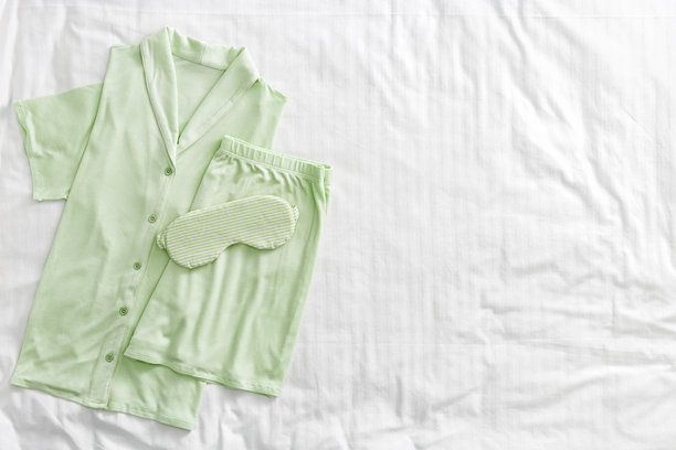 叠好的淡绿色女士睡衣和绸缎眼罩在白色床上的俯视图。极简风格的舒适睡衣，适合睡眠和放松。时尚睡衣的美学生活方式照片。图片下载