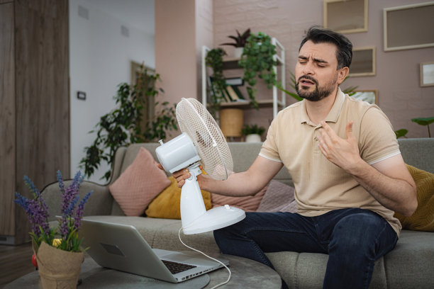 一名男子在家中因热浪而汗流浃背，正用风扇给自己扇风纳凉图片下载