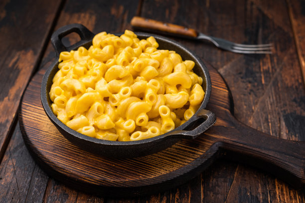 奶油芝士通心粉盛放在铸铁锅中，置于乡村风格的木桌上——一张充满慰藉感的食物照片。图片下载