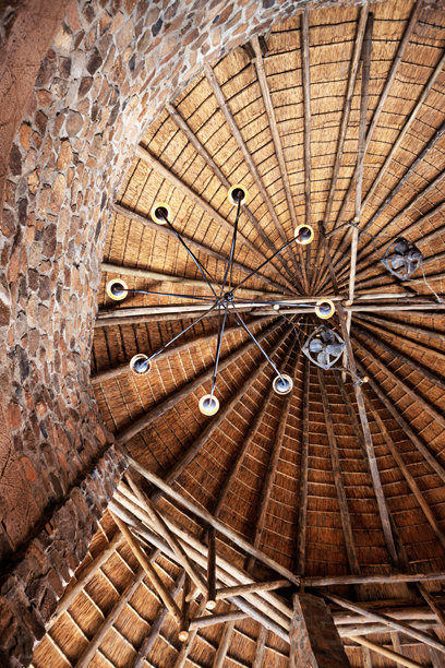 茅草屋顶悬挂的吊灯，配有巨大的木梁和复古工业风扇。设计见于圆形建筑、传统非洲茅屋。图片下载