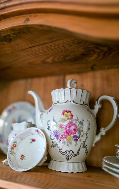 古董木柜架子上摆放着一些带有花卉设计和鎏金装饰的复古瓷茶具。图片下载