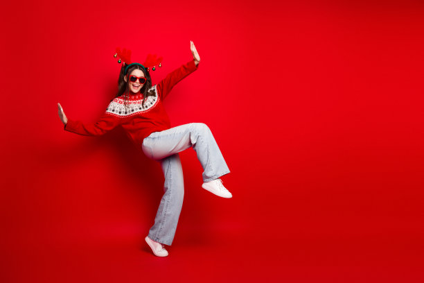 身穿红色圣诞毛衣的快乐女子在明亮的红色背景前跳舞，用于节日素材照片图片下载