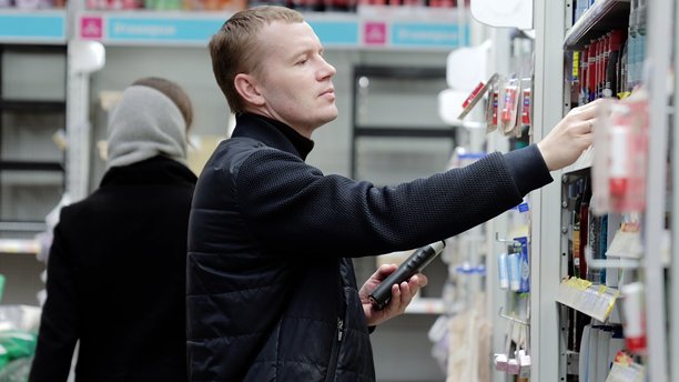 一名男子在超市购物时，使用智能手机应用程序比较产品，背景模糊了他的行走。一名男子在超市选择卫生用品，货架上摆满了洗发水。图片下载