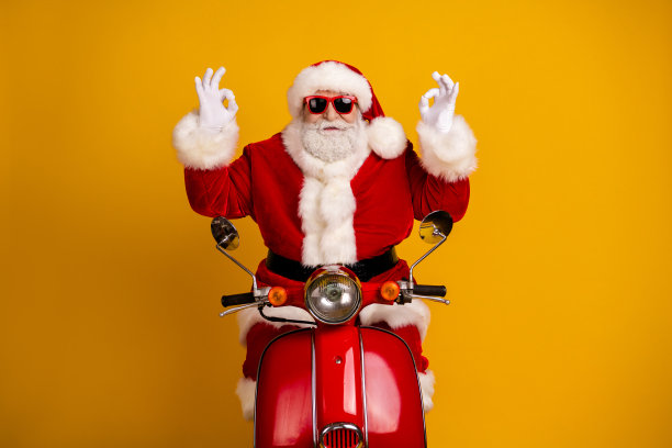 圣诞老人骑着红色踏板车，身穿节日毛衣、帽子和胡子，在黄色背景前摆姿势，用于节日圣诞主题的素材图。图片下载