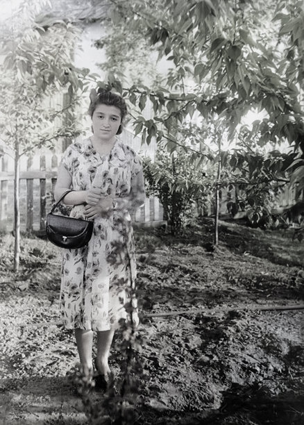 一位身着20世纪50年代时尚服装的年轻貌美女子在夏日花园中的复古肖像照，拍摄于1955年。图片下载