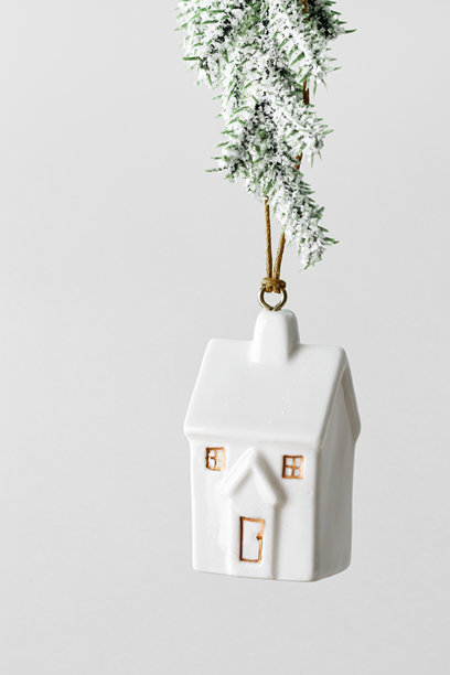 挂在雪枝上的小型房屋圣诞饰品，背景为灰色，象征着房产、抵押贷款、保险、新家和舒适假期的农历新年装饰，简约风格的冬季节日照片。图片下载