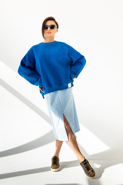 身穿蓝色运动衫和浅蓝色裙子的优雅女子，在白色背景前。时尚女性风格。工作室摄影。竖幅照片。图片下载