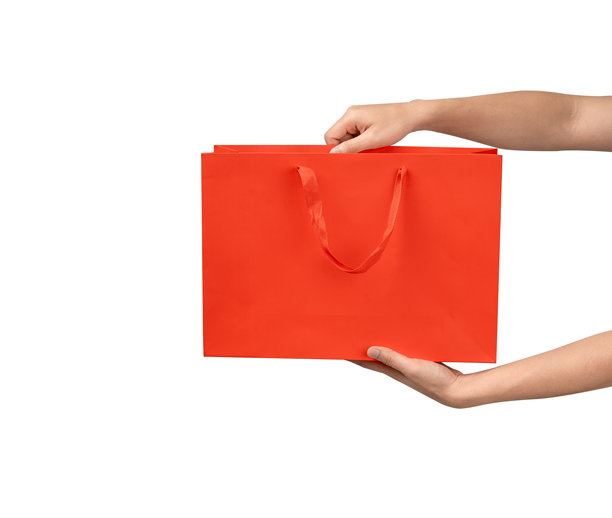 一只手拿着带提手的纸质购物袋，背景为干净的白色。工作室拍摄，有充足的复制空间用于文字、标志或品牌。在白色背景上隔离，抠出。图片下载
