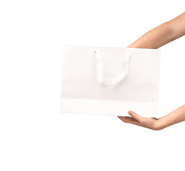 一只手提着带提手的纸质购物袋，背景为纯净的白色。工作室拍摄，留有充足的复制空间用于文字、标志或品牌宣传。白色隔离，抠图。图片下载