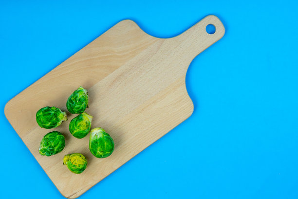 蓝底木质砧板上摆放着新鲜的抱子甘蓝，这是一张极简风格、以蔬菜为主题的产品照片图片下载