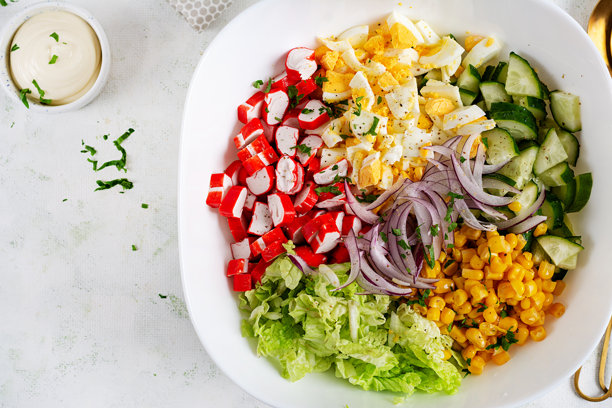 白碗里的沙拉，包含卷心菜、蟹肉棒、鸡蛋、黄瓜和红洋葱。健康沙拉。俯视图图片下载
