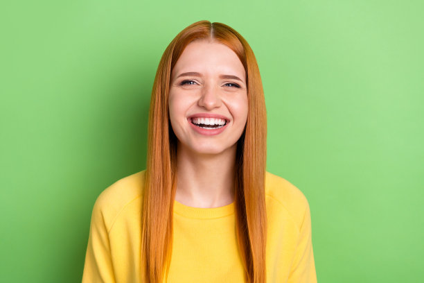 穿着黄色毛衣、留着橙色头发的甜美女士在淡绿色背景上开怀大笑的照片图片下载