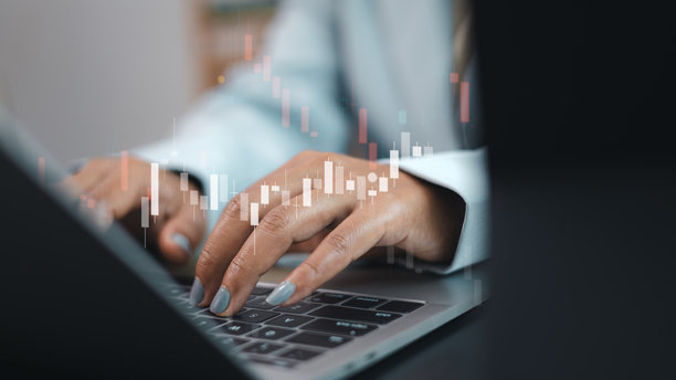 商务人士在笔记本电脑上打字，背景是股票市场的蜡烛图，象征着金融分析和交易概念。图片下载