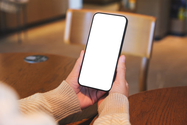 咖啡馆里，女子手持并使用手机，背景为空白的桌面屏幕的样机图图片下载