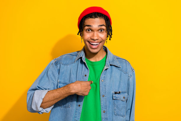 一名可爱的年轻男性照片肖像，他手指指向自己，显得很自信，穿着时尚的牛仔服装，在黄色背景上独立。图片下载