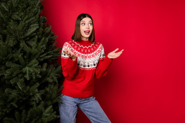 照片：一位穿着印花毛衣的漂亮年轻女子，双臂高举，望向虚空，背景为孤立的红色图片下载