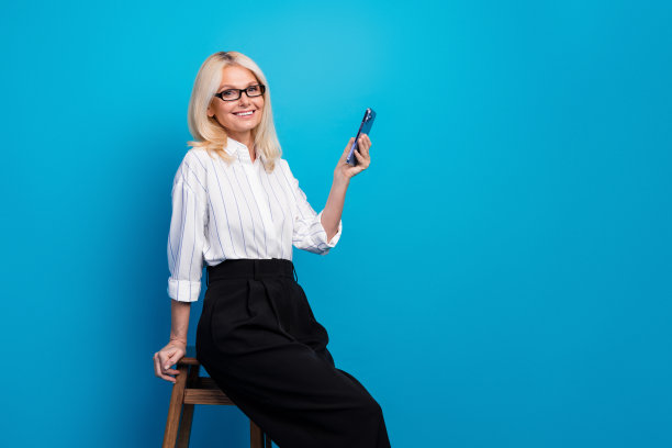 自信的女商人，身穿条纹衬衫和黑色裤子，在蓝色工作室手持智能手机，适合现代企业图库照片图片下载