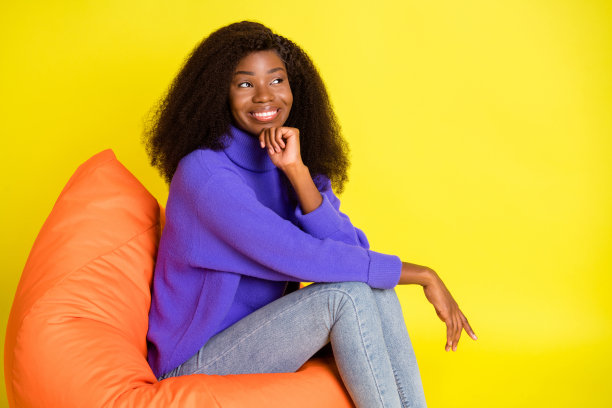 漂亮的深肤色女孩的头像，一只胳膊搭在下巴上，眼神空洞，露出灿烂的笑容，孤立在黄色的背景上图片下载