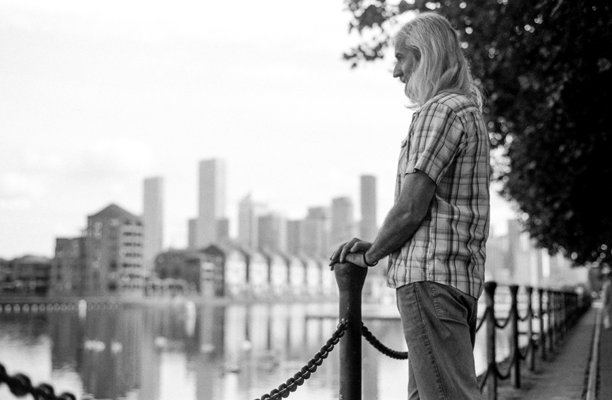 黑白照片：一位成熟男子在河边沉思城市天际线图片下载