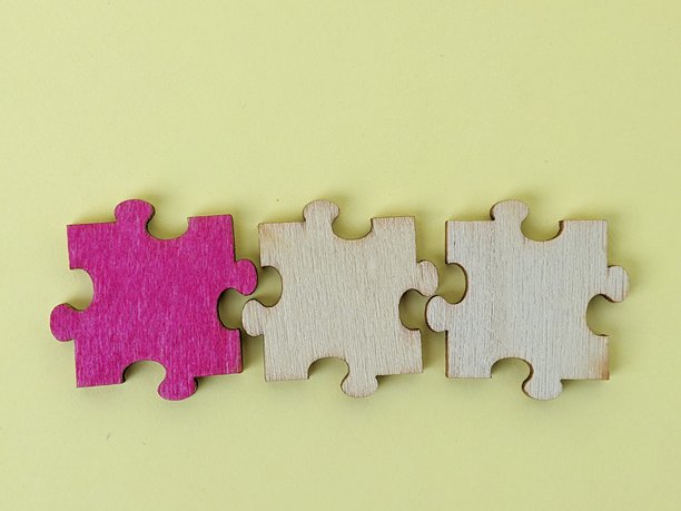 一排木制拼图块摆放在黄色背景上，第一个拼图块是粉红色的。这张图片传达了团队合作、协作和解决问题的概念，构图现代而多彩。图片下载