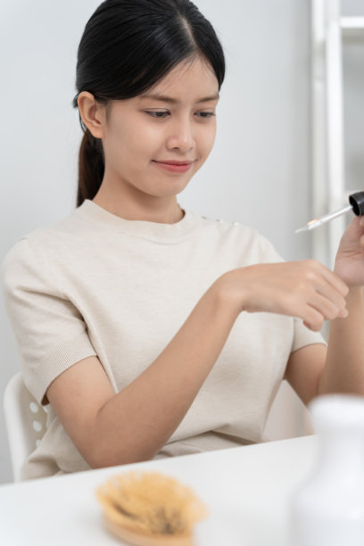 美丽的亚洲女性微笑着试用精华液，呵护肌肤。健康女性的面部涂抹面霜和化妆品。用于美白、保湿、抗皱、婴儿肌的护肤霜广告。图片下载