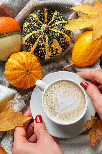 双手捧着咖啡，咖啡上是爱心拉花，周围环绕着秋季南瓜图片下载