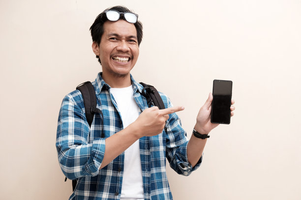 东南亚男子戴着眼镜，背着背包，展示手机屏幕并用手指指向图片下载