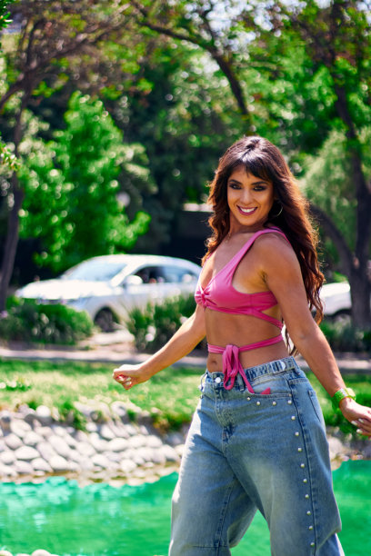 一位美丽的成熟拉丁裔阿拉伯棕发女郎在户外公园跳舞，身穿复古粉色服装和牛仔裤。图片下载