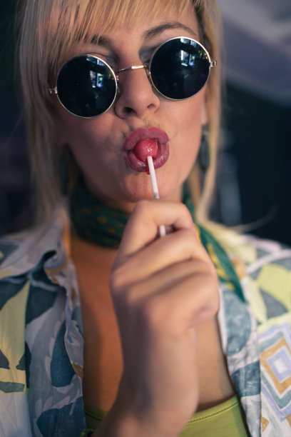 戴着复古太阳镜，享受棒棒糖的俏皮金发女郎图片下载