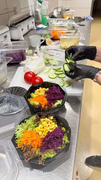 戴黑色手套的手在不锈钢厨房台面上摆放外卖碗里的健康蔬菜沙拉，配有胡萝卜、玉米和紫甘蓝。专业照片图片下载