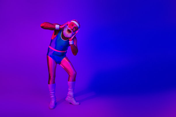 身穿复古运动服的老年男子摆出俏皮的姿势，在紫蓝色霓虹灯下，营造出有趣、充满活力的健身生活方式素材照片图片下载