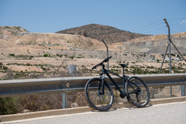 山地自行车停靠在公路护栏上，背景是风景优美的沙漠山丘图片下载