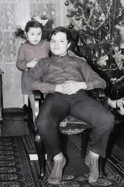 一张复古风格的姐妹和兄弟在新年树旁的肖像照。一个戴着蝴蝶结的女孩拥抱着她的弟弟。摄于1973年。图片下载