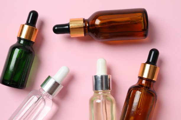 使用化妆品面部精华液进行皮肤护理。彩色背景上的滴管玻璃瓶。干性皮肤护理产品。用于滋润身体皮肤的精油。图片下载