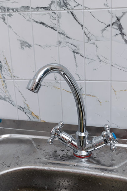 大理石瓷砖背景下，现代不锈钢厨房水龙头正在放水图片下载