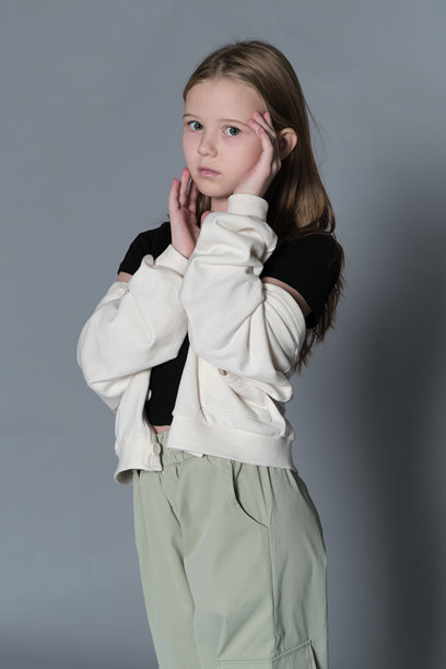 一个穿着黑色上衣和绿色裤子的年轻女孩侧身站着，眼神看着镜头。这张照片捕捉了青春的温柔和沉思的本质，定格在宁静的瞬间。图片下载