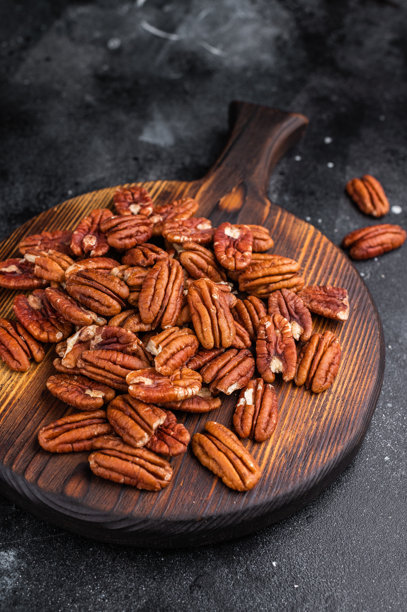 原味山核桃仁散落在质朴的木板上，背景为深色纹理，营造出温馨的美食场景，非常适合烹饪类素材使用图片下载