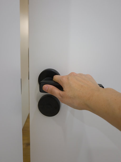 一只手正在打开一扇带有黑色把手的白色门，突显了进入或离开现代室内空间的动作。这张照片捕捉了一个日常瞬间，强调了通行和过渡。图片下载