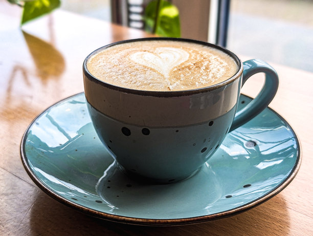 木制桌上，一个绿松石色陶瓷杯中的卡布奇诺咖啡，咖啡表面有心形拉花特写图片下载