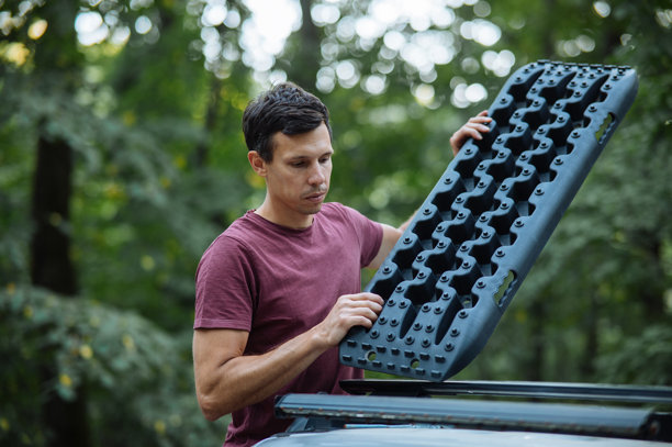 男人在森林中将越野救援板放在汽车车顶上。图片下载